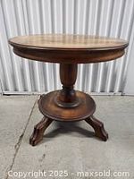 Front view of the entire round wood side table showing the pedestal base and three legs.