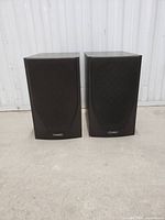 Front view of pair of black Mission M72 bookshelf speakers with fabric grills in place, showing logo near bottom.
