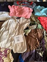 Overview of assorted women’s clothing including pleated blouse, striped and pink tees, tan pants, patterned garments