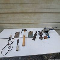Overview of assorted hand tools, grinding wheels, vise, punch sets, hammer, plane and rod on table