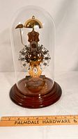 Front view of Kieninger brass skeleton clock under glass dome on wooden base