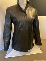 Front of black leather jacket on mannequin showing standing collar and concealed placket