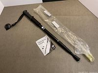 Full view of trekking pole with strap, rubber tip, instructions, plastic sleeve