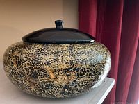 Front view of lacquerware vessel showing gold and black pattern and black lid