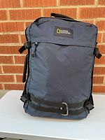 Front view showing National Geographic logo, navy nylon body, front zip pocket, compression straps, D-ring