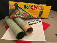 Box front and contents including rolled green felt mat, cardboard tube, straps