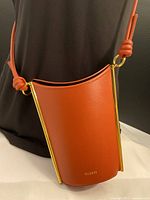 Front view of burnt-orange Yuzefi leather purse with gold side bars and knotted strap