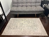 Full view of the black, grey, and white area rug placed below a grey sofa and black side table on dark hardwood floor.