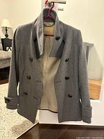 Front view of grey double-breasted peacoat on hanger showing buttons, collar, and pockets.