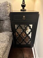 Black solid wood end table positioned beside a sofa with a lamp on top