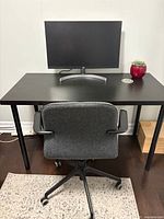 Front view of black wooden desk with black metal legs, monitor and gray office chair pictured but not included