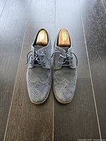 Top-down view of both blue leather brogue dress shoes placed side by side on dark floor showing laces, perforation pattern, and shoe shape.