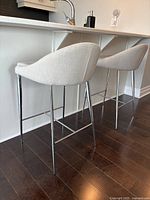 Side view of 2 light gray fabric counter stools with chrome legs under a kitchen counter.