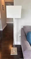 Floor lamp full view from front showing brushed nickel base and stem with white rectangular shade near sofa.
