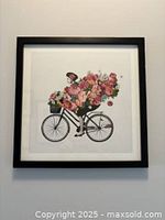 Frontal image of the framed art print titled 'Flower Girl' depicting a Parisian woman on a bicycle with abundant flowers, showcasing the black frame and white mat.