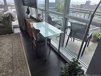 Desk placed near floor-to-ceiling glass windows with city view, showing the glass top and two metal legs connected to a thin frame.