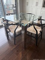 Dining table shown with cushioning chairs around, glass top clean and shiny, legs chrome and reflective.