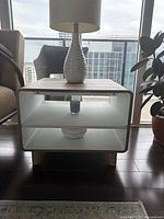Front view of the grey and white end table with a lamp and diffuser on the shelf, showing the interior white shelf and exterior woodgrain.