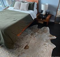 Cowhide rug placed on dark hardwood floor next to a bed, showing full pattern and gold inlay effect clearly.