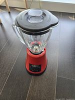 Red Oster blender with transparent glass pitcher and black lid, showing base and control panel.