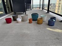 Wide view of all 10 pots arranged in a row on outdoor concrete floor showing variety of colors and sizes.