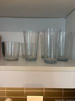 6 tall and 4 short ribbed clear water glasses on shelf, arranged side by side.