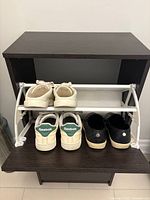 Front view of shoe cabinet with lower compartment open showing 4 pairs of shoes inside on white racks.