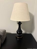 View of the wooden table lamp with fabric shade unlit on a black surface next to gray upholstered furniture.
