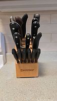 Front view of wooden knife block with 16 knives, showing black plastic handles and wood handles, Wusthof branding visible on block.