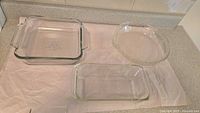 Three clear glass bakeware dishes: square casserole dish with handles, rectangular loaf pan, and round pie dish, displayed on counter.