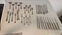 Full flatware set laid out on countertop showing all spoons, forks, dessert forks, butter knives, and steak knives.