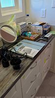 Vanity mirror, digital scale, boxed toiletries, and black hair dryer with cords on bathroom counter