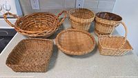 Full view of the 6 assorted wicker baskets on a kitchen counter, showing variety of sizes and styles.