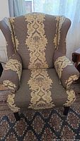 Front view of brown fabric armchair with gold/tan Baroque floral pattern, cushioned seat, and curved armrests.