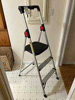 Side view of the Benchmark aluminum folding ladder showing three wide steps and black plastic top handle.