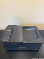 Side-angle view of Canon TR4527 all-in-one printer showing keypad, display, and paper tray.