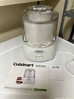 Front view of Cuisinart ICE-20C frozen yogurt maker with clear lid in place and instruction manual booklet beside it