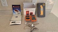 Overview of set including Starfrit kitchen scale, ThermoPro TP-20 thermometers in orange, Thermapen Mk4 thermometer box, and probes with clips laid out on countertop.