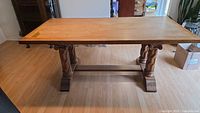 Front view of wooden farmhouse dining table with double pedestal trestle legs and a natural wood finish top, showing overall design.