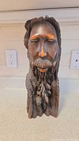 Front view of the hand-carved wooden sculpture showing detailed facial features and braided beard of the human figure.