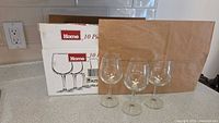 Photo of 3 glass wine stemware glasses in front of their original Home brand packaging box on a kitchen counter.