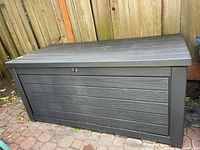 Front angle view of closed deck box on brick patio against wooden fence