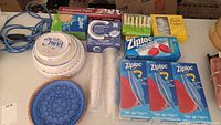 Top-down image showing an assortment of paper plates, blue plastic plates, wicker baskets, parchment paper, boxes of Ziploc bags, and yellow plastic cutlery.