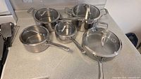 Photo showing entire set on counter: four pots/pans with five glass lids, stainless steel finish