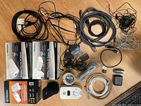 All items on a wooden surface showing 3 TRENDnet Powerline AV Adapter Kits in boxes, assorted cables, power strip, headphones, Chromecast, power adapters, wall plug, digital thermostat or CO detector, and additional small accessories.