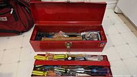 Red metal Mastercraft tool box open showing various tools inside and additional hand tools spread in front.