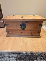 Front view of the wooden chest showing metal latch and decorative hinges on the lid and front.