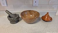 Photo shows all three items: the mini tagine lid and base, the brown glazed bowl, and the granite mortar and pestle on a countertop.