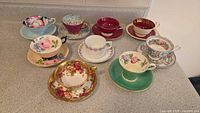 Nine assorted teacup and saucer pairs arranged on countertop