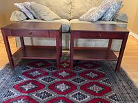 Front view showing the pair of dark cherry stain composite wood end tables with one drawer and lower shelf each.